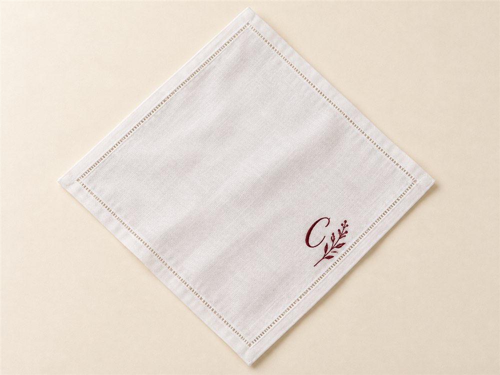 White handkerchief with a fictional burgundy embroidered initial and botanical sprig