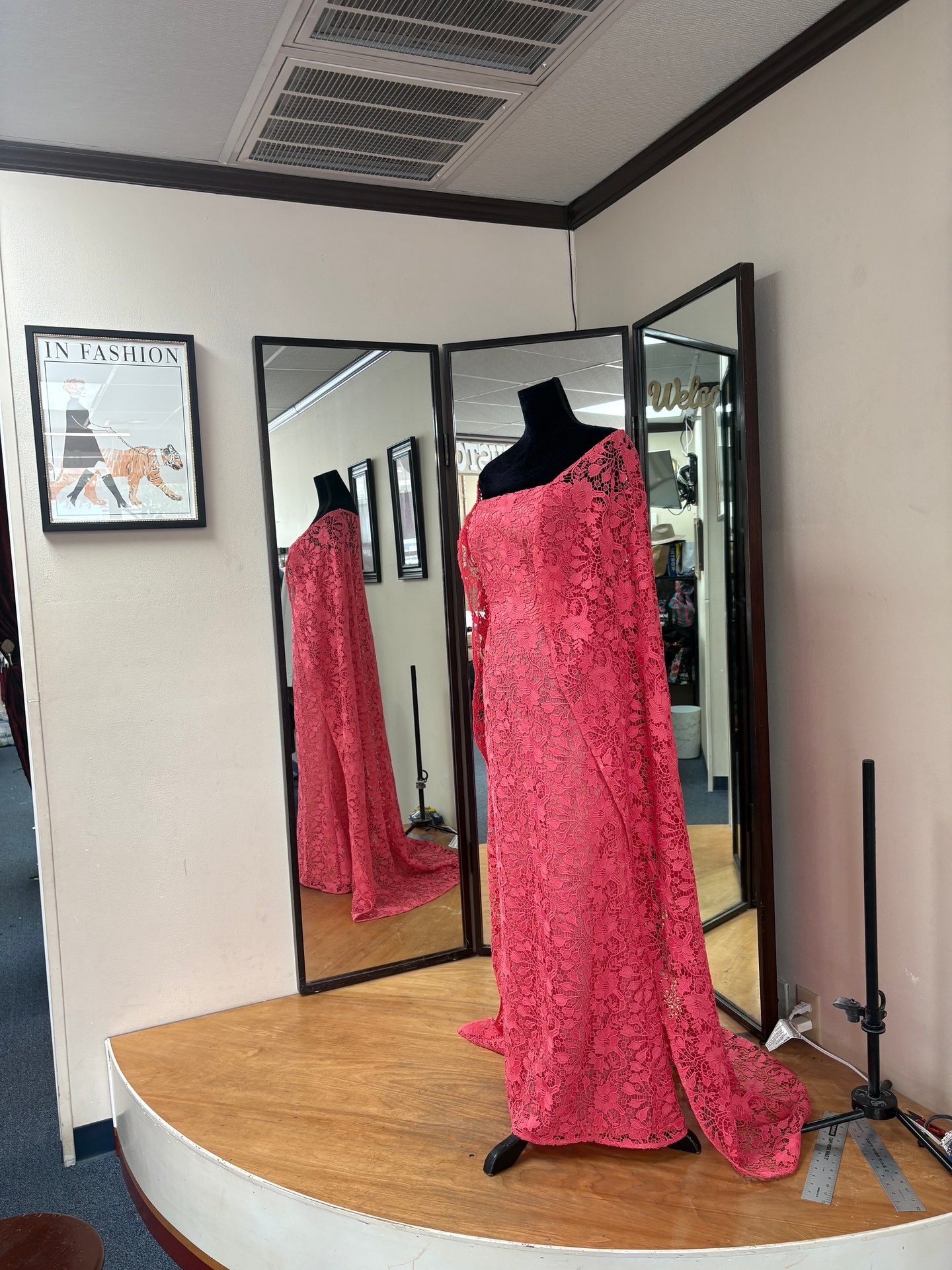 Full-length coral-pink lace gown with an angled neckline and extended lace panels reflected in fitting-room mirrors