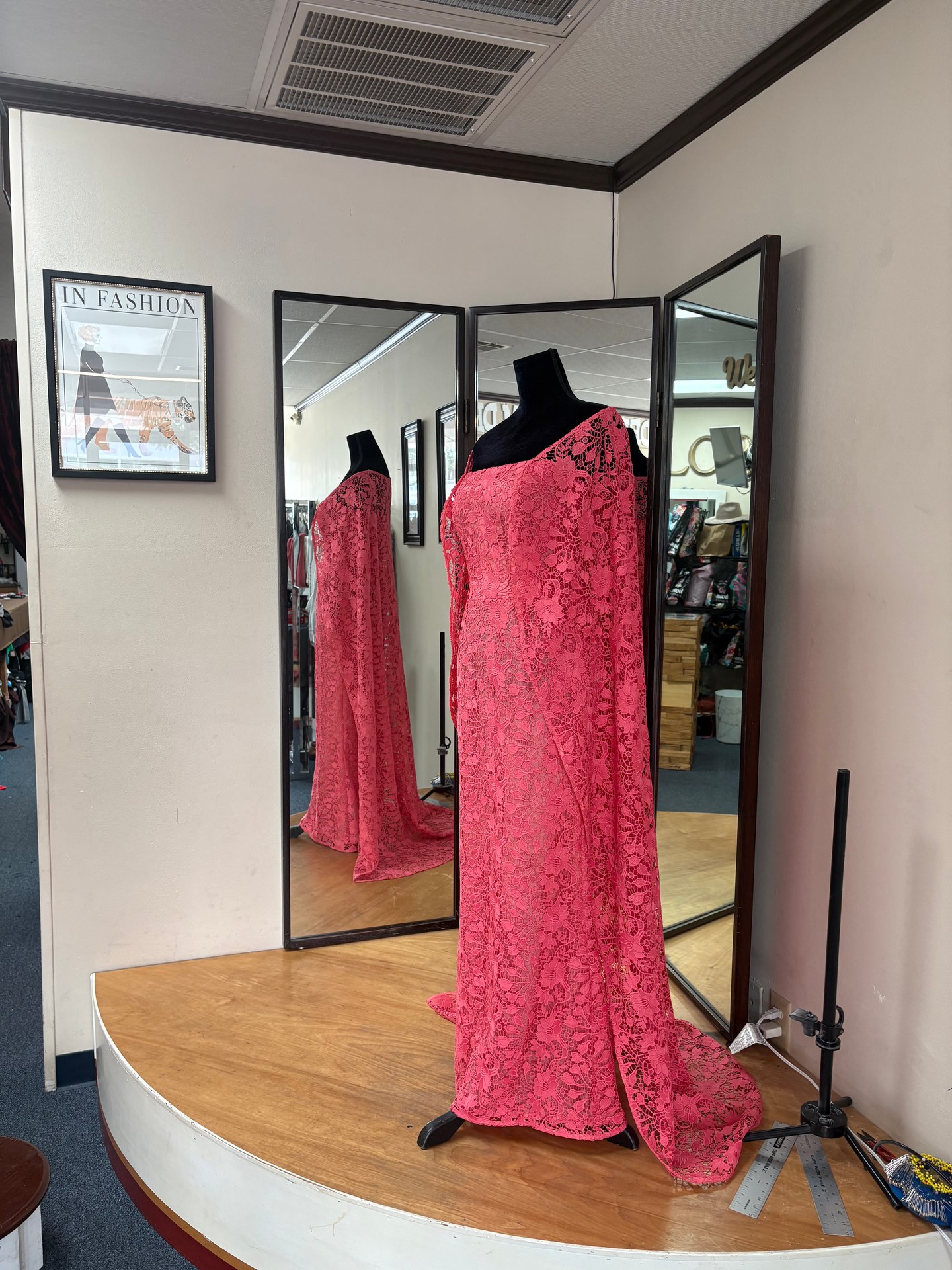 Side view of the coral-pink floral lace gown showing its long cape-style drapery and floor-length silhouette