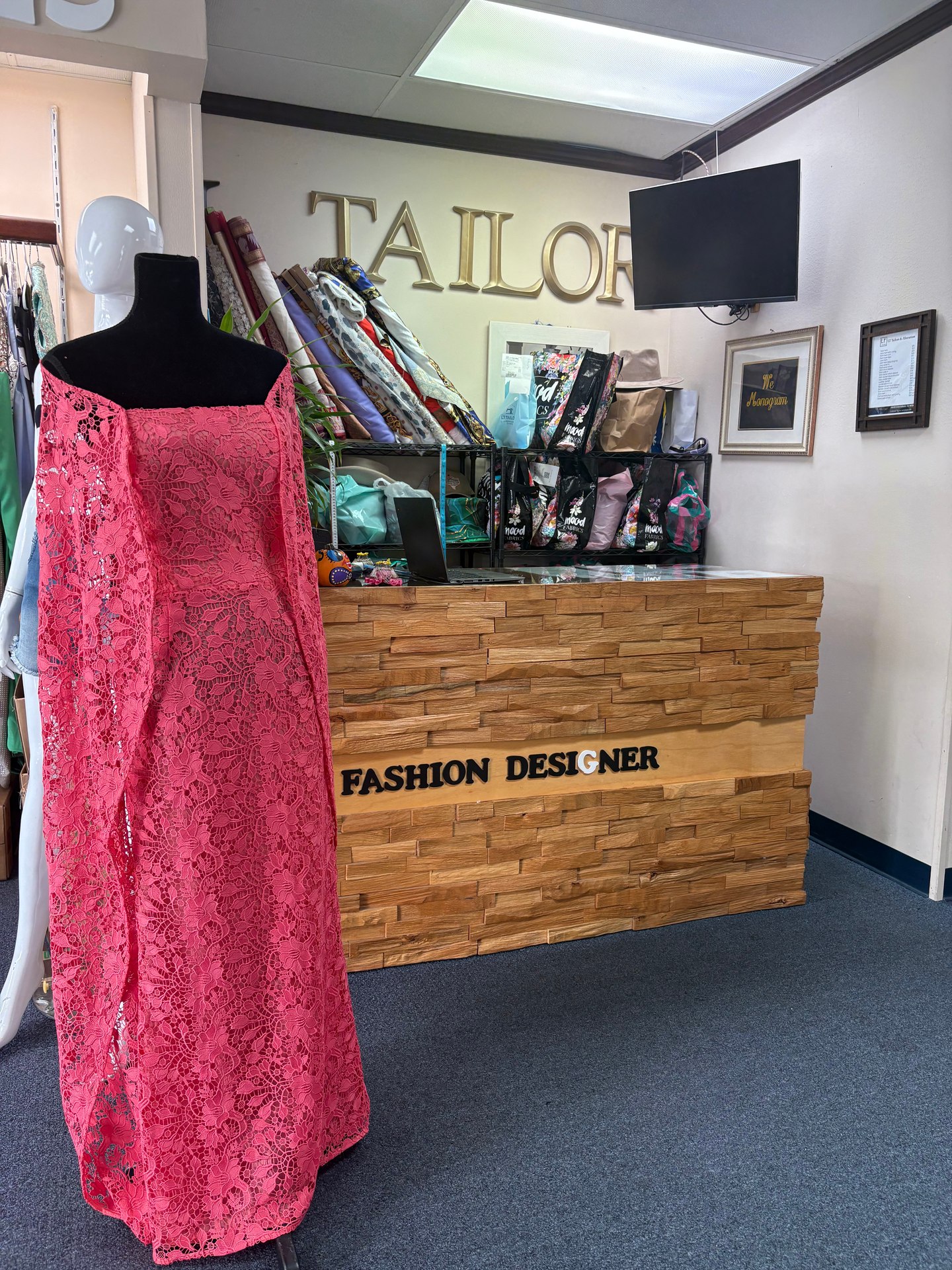 Custom coral-pink floral lace evening gown with flowing drapery displayed beside the LT Tailors shop counter